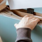 Total Quality Management - Crop anonymous male putting blank sheet of paper in case placed on wooden table