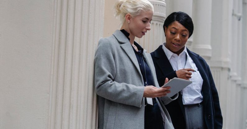 Break-Even Analyses - Well dressed young multiethnic female colleagues using tablet while discussing project on street