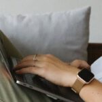 Project Casebook - Side view of crop unrecognizable female freelancer in casual clothes and smartwatch lying on comfortable sofa and working remotely on laptop